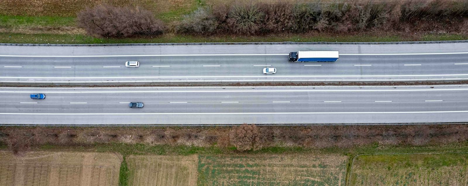 Vue aérienne d’une autoroute traversant des champs, avec un poids lourd en circulation